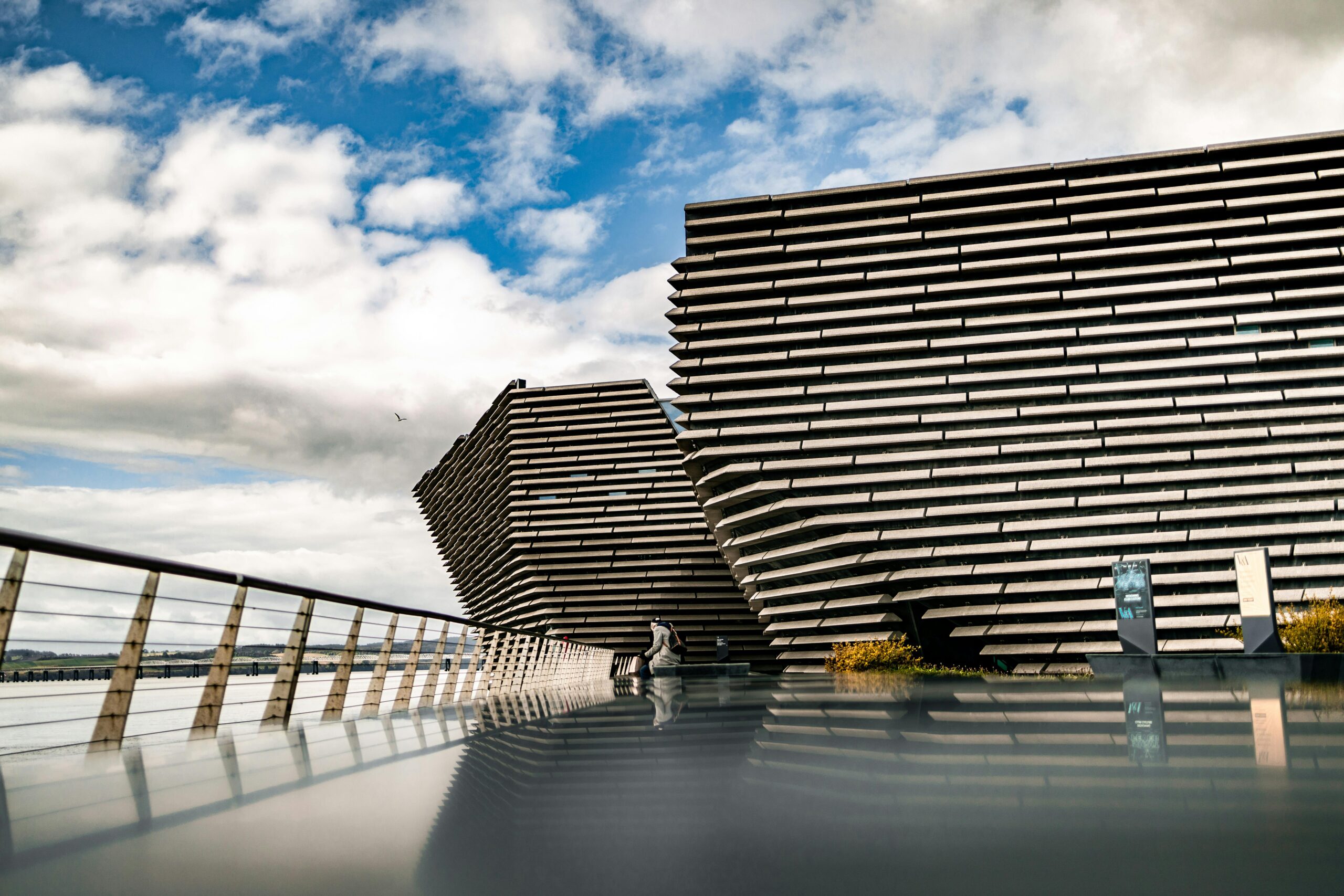 The striking modern architecture of V&A Dundee along the riverside in Scotland with a reflective foreground.